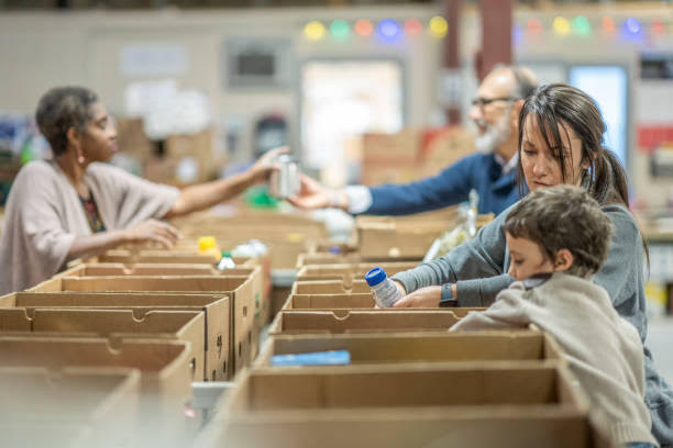 Many people are placing food items into empty boxes lined up on a table.